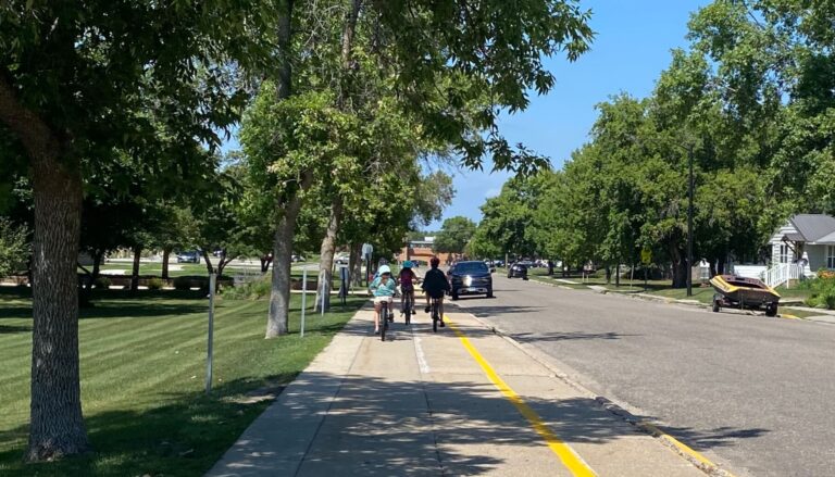 Kids riding bikes on the side walk to school on a sunny day.
