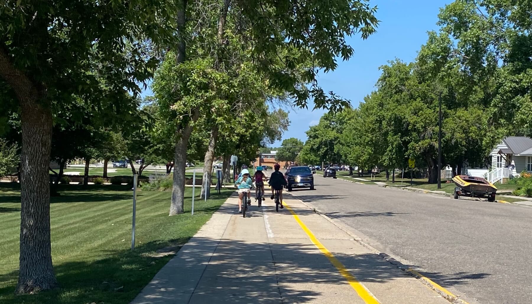Kids riding bikes on the side walk to school on a sunny day.