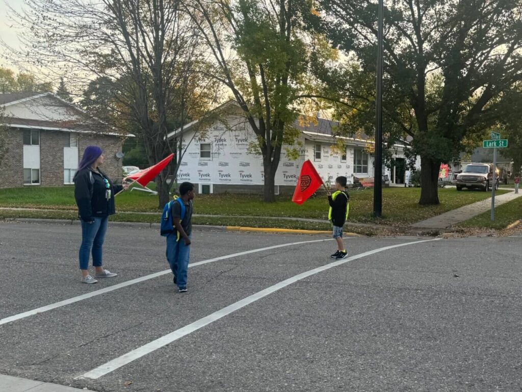 Two kids and one adult holding red flags in a crosswalk.