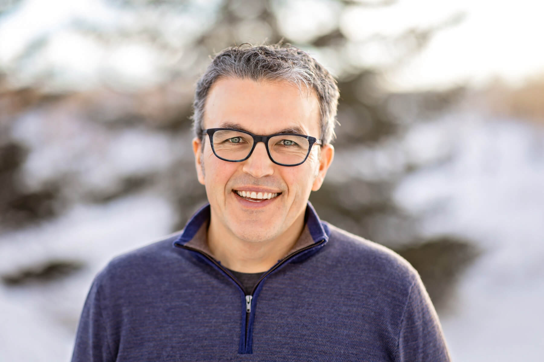 Ryan Rooney stands outside on a snowy day. He is smiling. He is wearing a blue quarter-zip sweater and glasses. He has short salt-and-pepper hair.