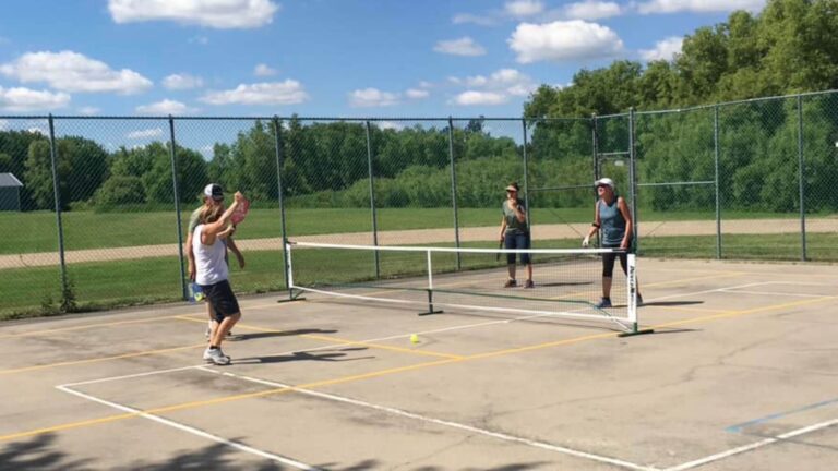 Three people are playing pickleball on a pickleball court. They are holding pickleball paddles and celebrating winning a point. The courts have a net and chain link fence around them.