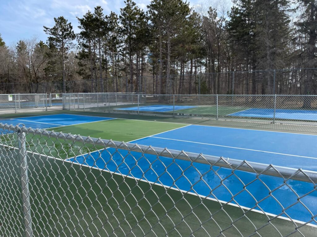 There are four blue pickleball courts. A chain link fence surrounds the courts.