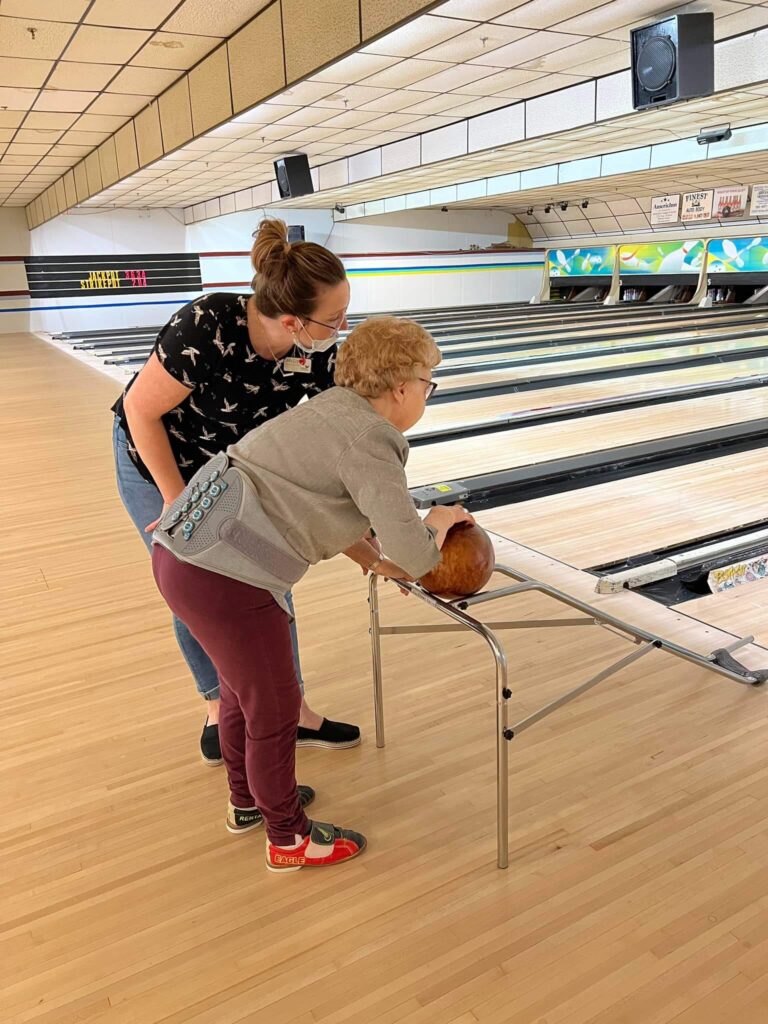 Caretaker and older woman bowling